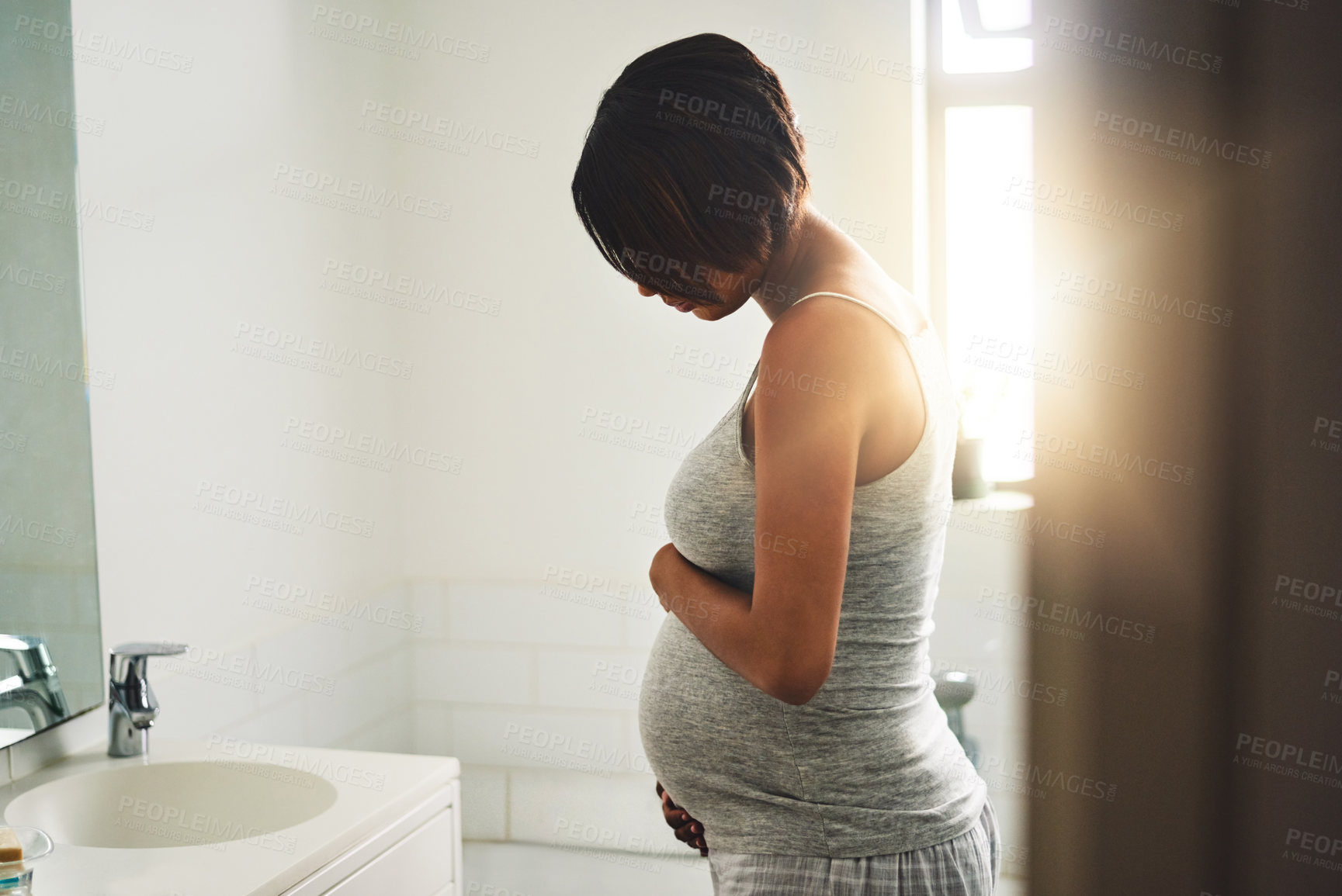 Buy stock photo Shot of a pregnant young woman standing in the bathroom at home
