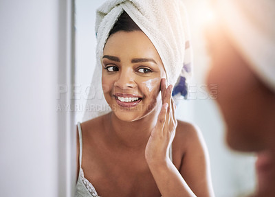 Buy stock photo Shot of an attractive young woman applying moisturizer to her face in the bathroom