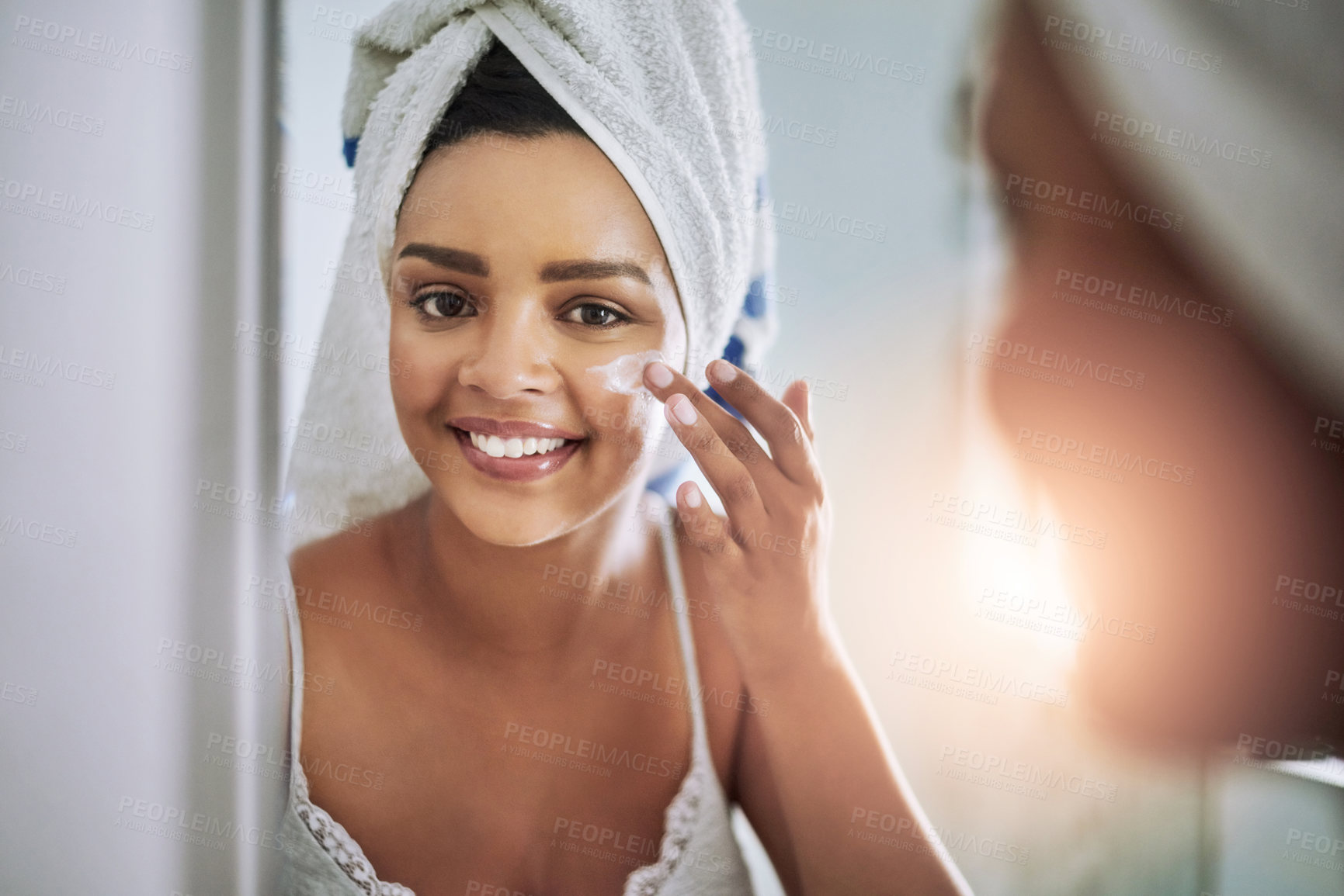 Buy stock photo Portrait of an attractive young woman applying moisturizer to her face in the bathroom