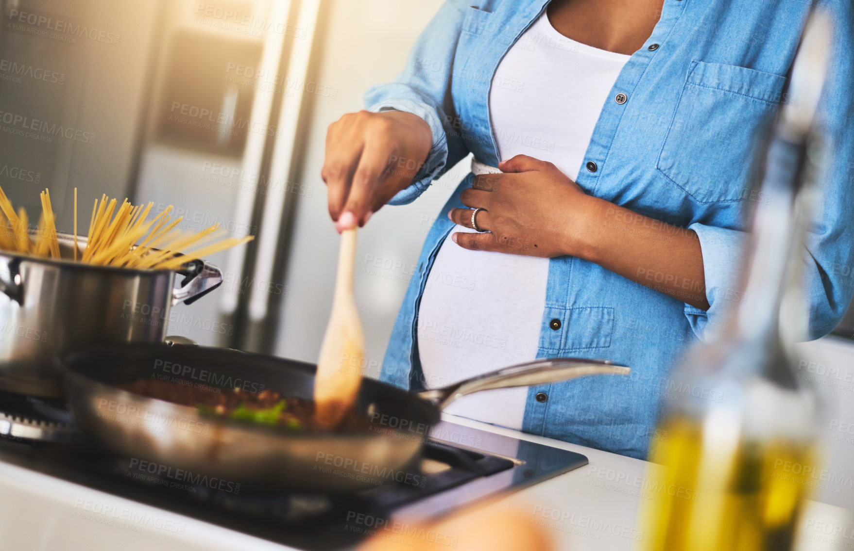 Buy stock photo Cropped shot of a pregnant woman preparing a meal on the stove at home