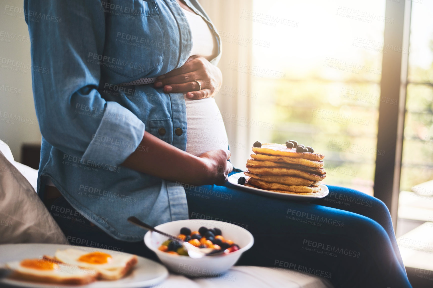 Buy stock photo Cropped shot of a pregnant woman eating delicious pancakes at home