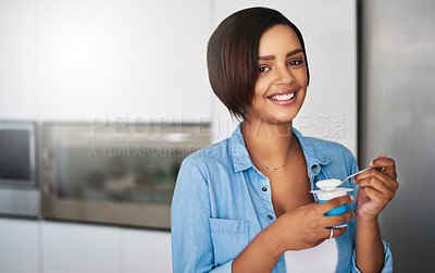 Buy stock photo Shot of an attractive young woman eating a tub of yoghurt at home