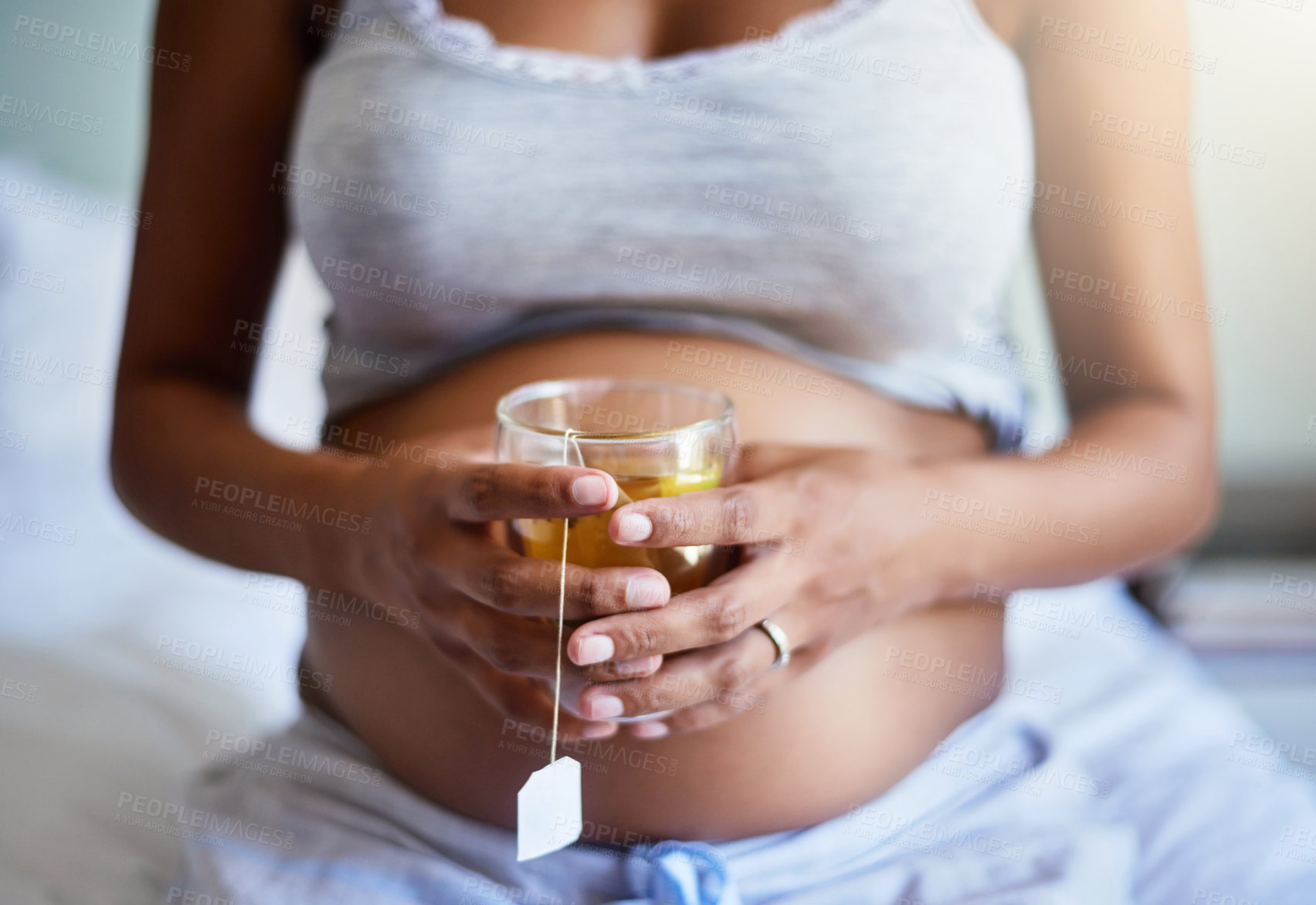 Buy stock photo Cropped shot of a pregnant woman relaxing at home with a glass of tea