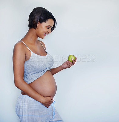 Buy stock photo Studio shot of an attractive young pregnant woman holding a green apple