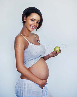 Buy stock photo Studio shot of an attractive young pregnant woman holding a green apple