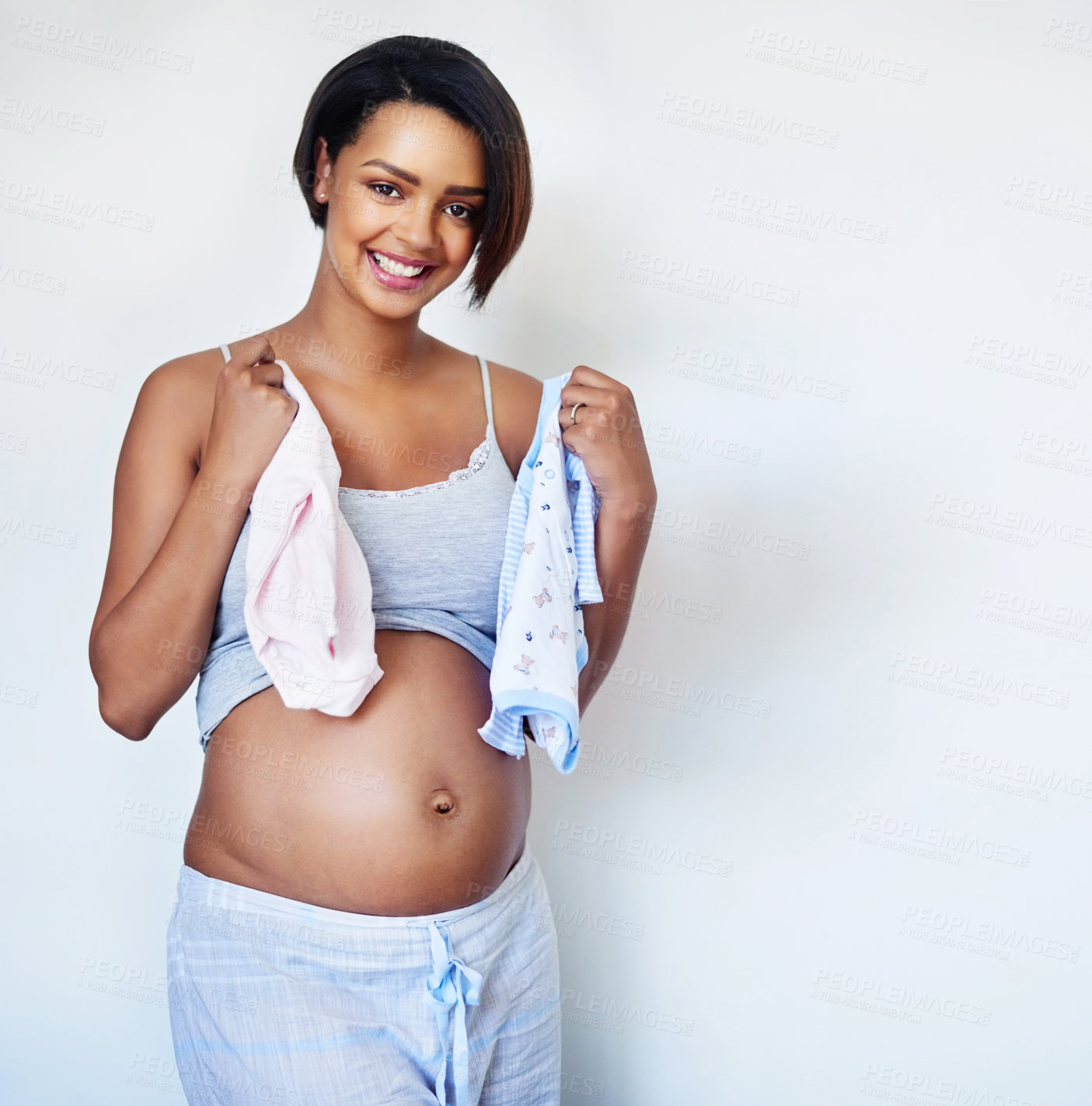 Buy stock photo Studio shot of an attractive young pregnant woman holding pink and blue baby clothes