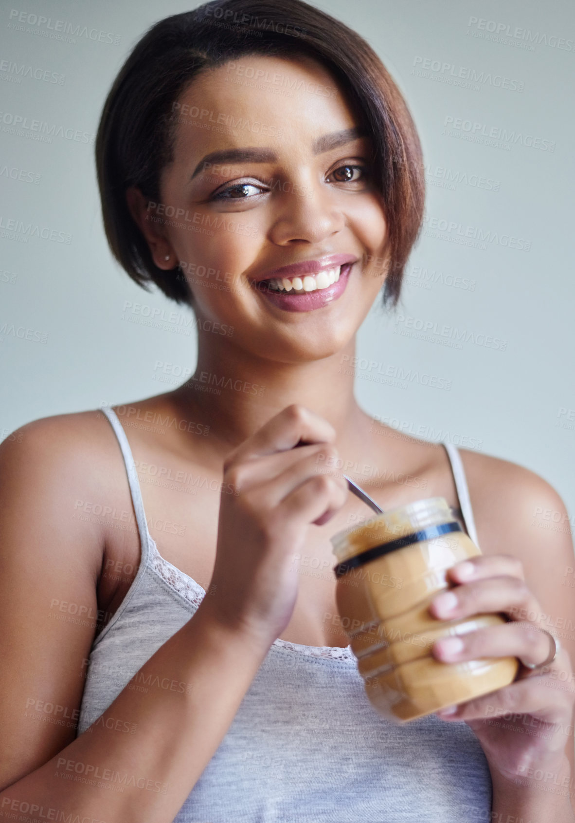 Buy stock photo Studio shot of an attractive young woman eating from a jar of peanut butter against a gray background