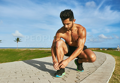 Buy stock photo Shot of a handsome young man tying his shoelaces while exercising outdoors