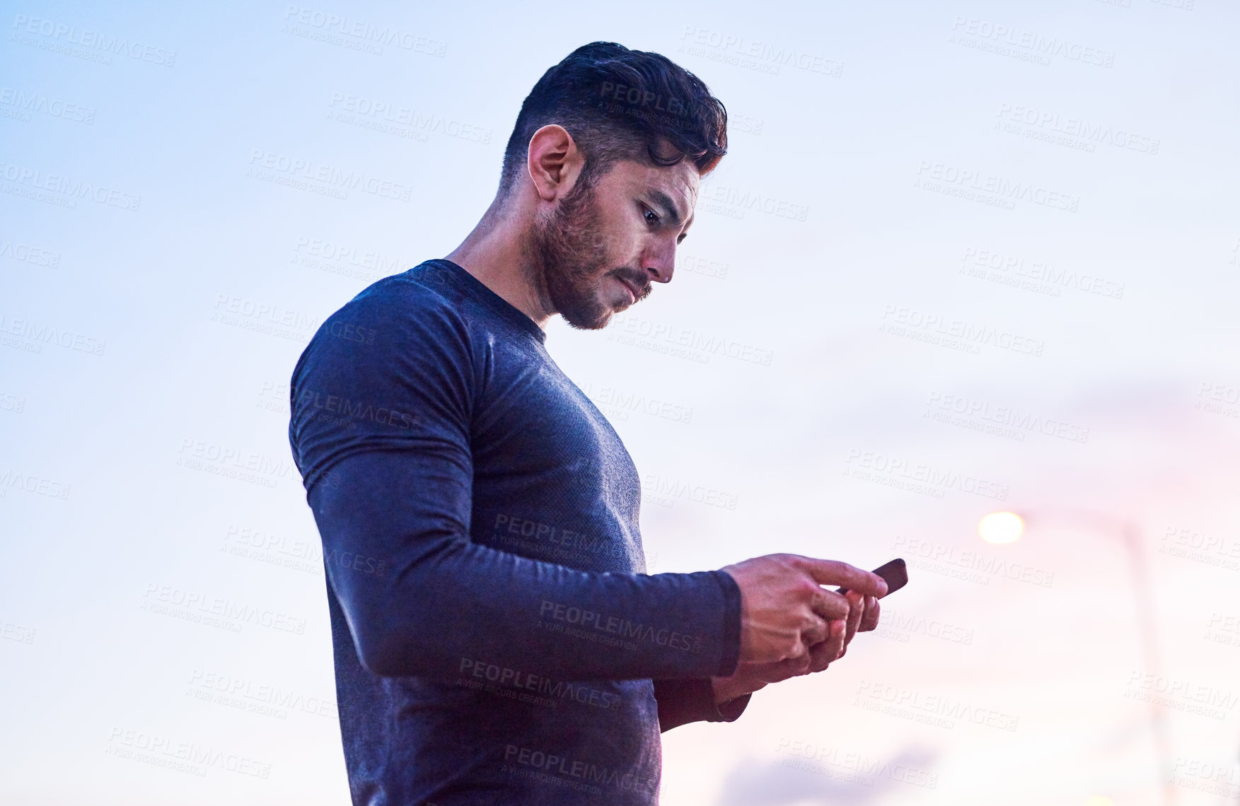 Buy stock photo Shot of a sporty young man using a cellphone outdoors