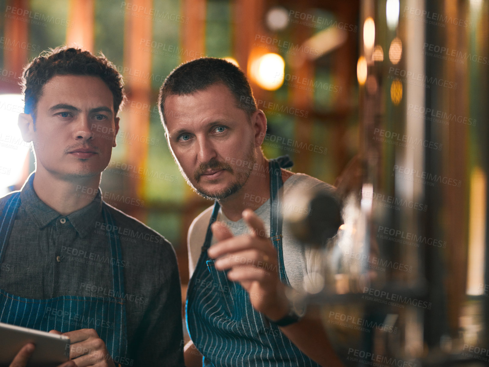 Buy stock photo Shot of two young working men doing inspection of their beer making machinery inside of a beer brewery during the day