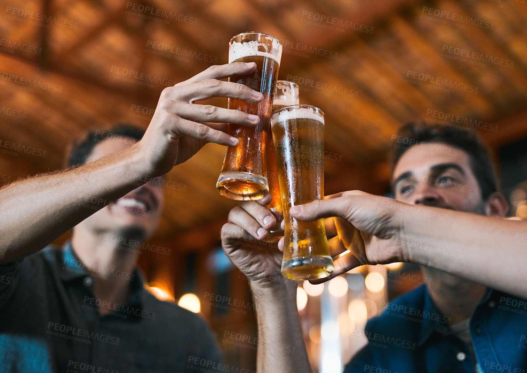 Buy stock photo Shot of three cheerful young men having a celebratory toast with beer while sitting at a table inside of a beer brewery during the day