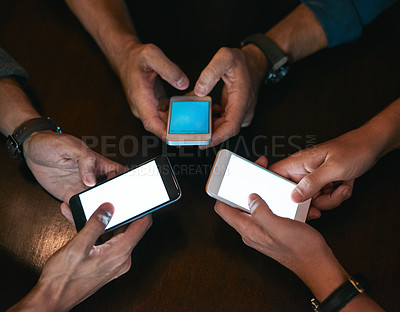 Buy stock photo High angle shot of three unrecognizable people seated in a circle at a table while browsing on their cellphones