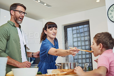 Buy stock photo Shot of a mother giving her son a taste of the meal that she's cooking at home
