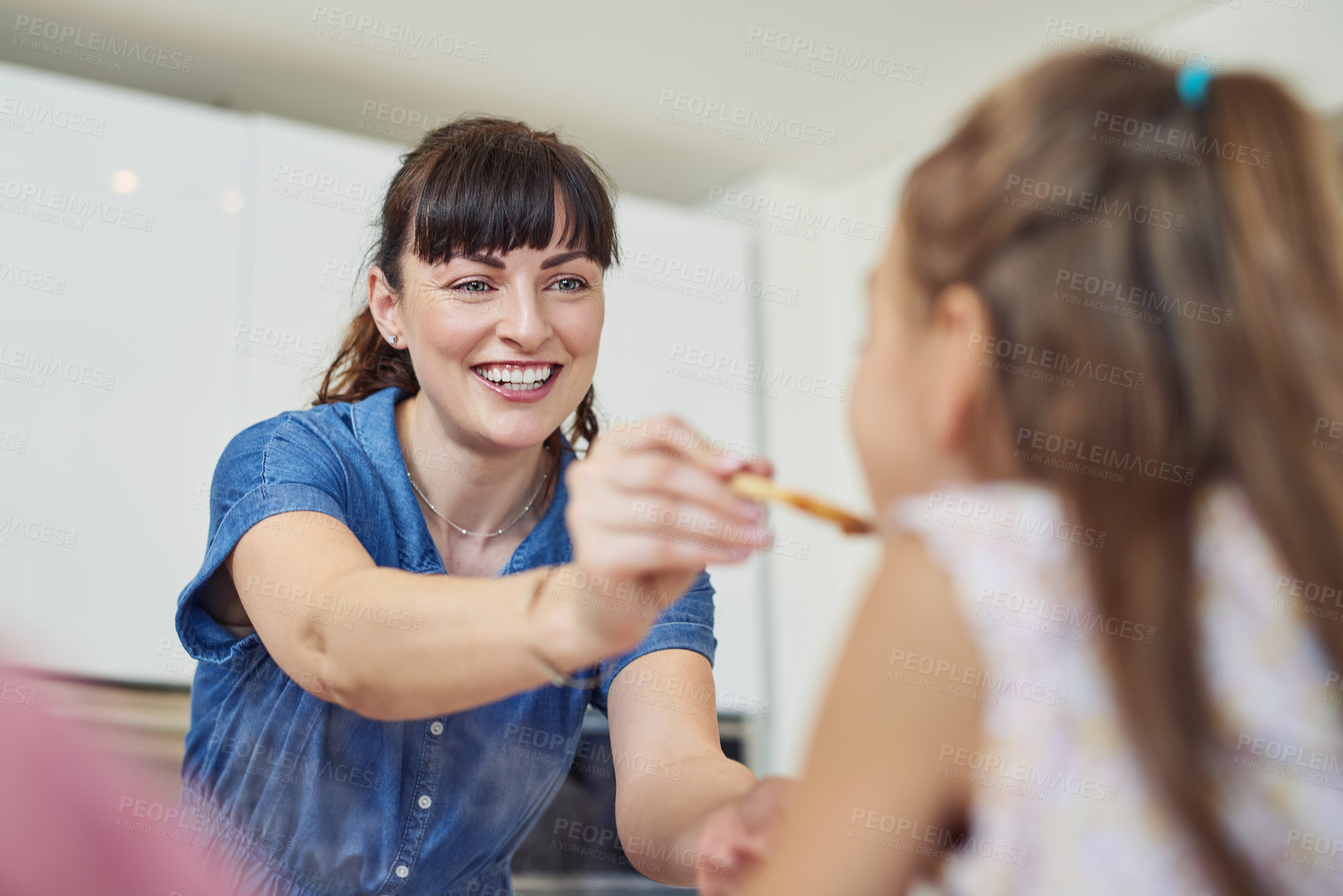 Buy stock photo Shot of a mother giving her daughter a taste of the meal that she's cooking at home