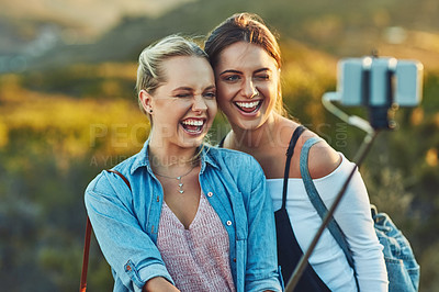 Buy stock photo Cropped shot of two beautiful female friends taking a selfie using a selfie stick in nature