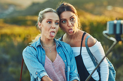 Buy stock photo Cropped shot of two beautiful female friends taking a selfie using a selfie stick in nature