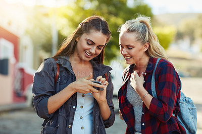 Buy stock photo Cropped shot of two beautiful female friends using a cellphone together in the city