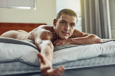 Buy stock photo Portrait of a cheerful young man lying on his stomach while being naked on the bed and stretching his arm out to the camera