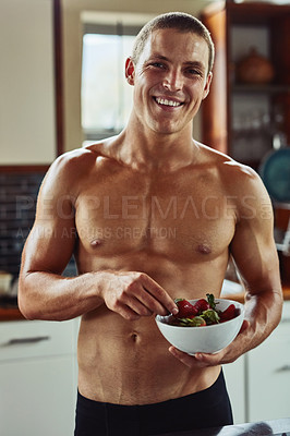 Buy stock photo Portrait of a cheerful young man  wearing only his underwear while enjoying a bowl of strawberries in the kitchen at home