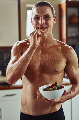 Buy stock photo Portrait of a cheerful young man  wearing only his underwear while enjoying a bowl of strawberries in the kitchen at home
