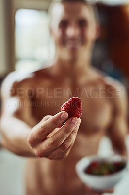 Buy stock photo Closeup of a cheerful young shirtless man holding out a strawberry at the camera at home during the day