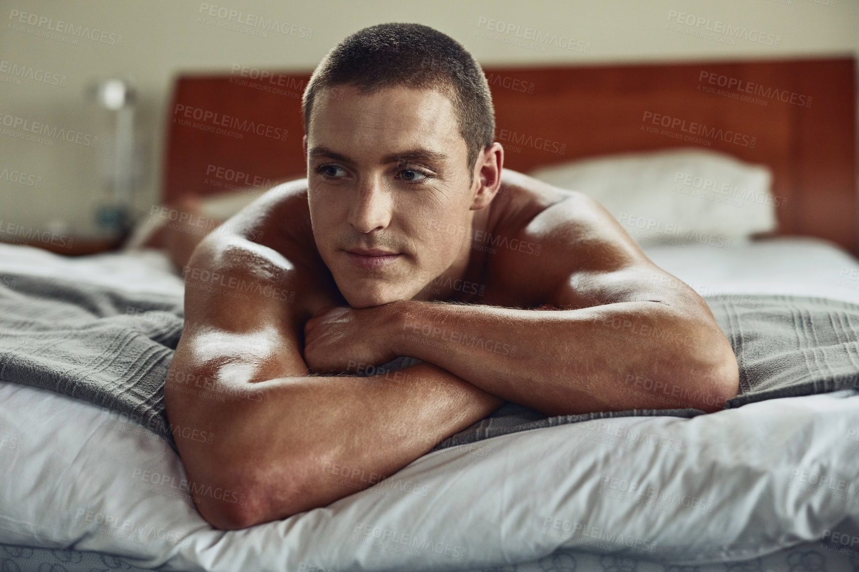 Buy stock photo Shot of a carefree young naked man lying on his bed with his arms folded at home during the day