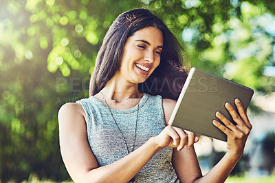 Buy stock photo Shot of an attractive young woman using a digital tablet outdoors