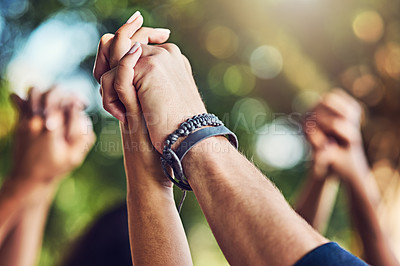 Buy stock photo Closeup shot of an unrecognizable group of people holding hands with their arms raised outdoors