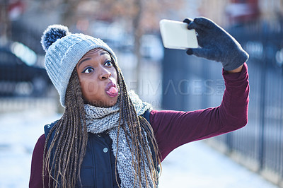 Buy stock photo Shot of a beautiful young woman taking a fun selfie on a snowy day outdoors
