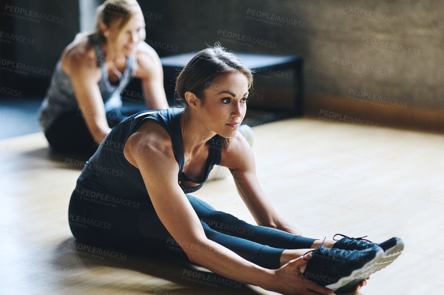 Buy stock photo Full length shot of two attractive young women stretching before their workout in the gym