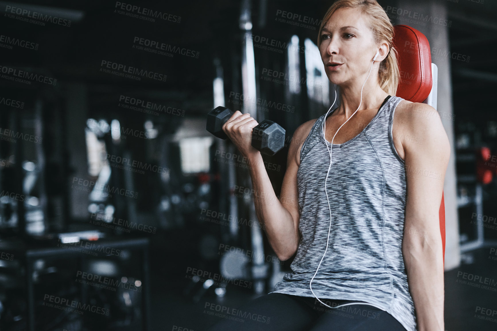Buy stock photo Cropped shot of an attractive young woman listening to music while working out with a dumbbell in the gym
