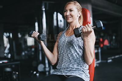 Buy stock photo Cropped shot of an attractive young woman listening to music while working out with dumbbells in the gym