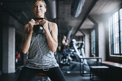 Buy stock photo Cropped shot of an attractive young woman listening to music while working out with a kettle bell in the gym