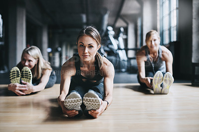 Buy stock photo Full length shot of three attractive and athletic women stretching before their workout in the gym