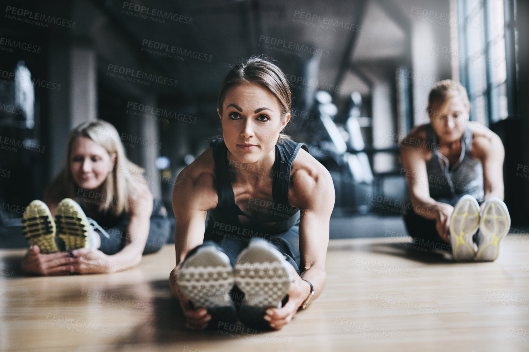 Buy stock photo Full length shot of three attractive and athletic women stretching before their workout in the gym