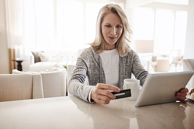 Buy stock photo Shot of a mature woman using a credit card and digital tablet while relaxing at home