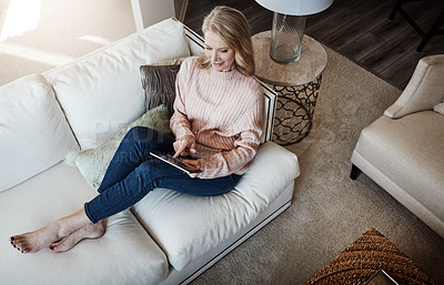 Buy stock photo Shot of a mature woman using a digital tablet while relaxing on the sofa at home