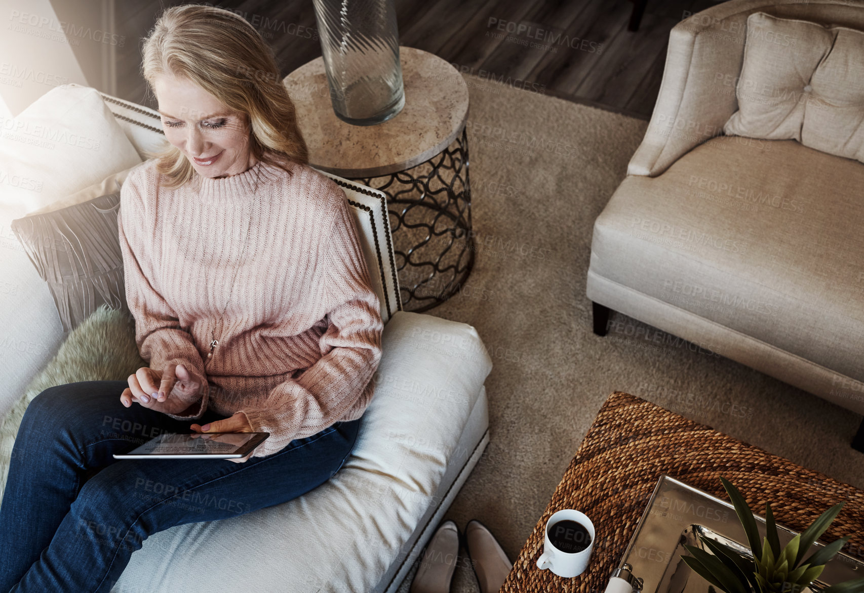 Buy stock photo Shot of a mature woman using a digital tablet while relaxing on the sofa at home