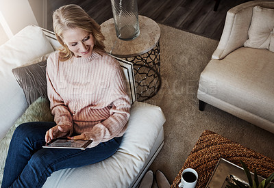 Buy stock photo Shot of a mature woman using a digital tablet while relaxing on the sofa at home