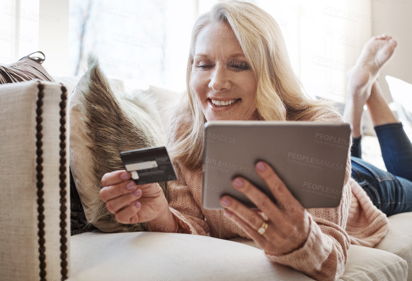Buy stock photo Shot of a mature woman using a credit card and digital tablet while relaxing at home