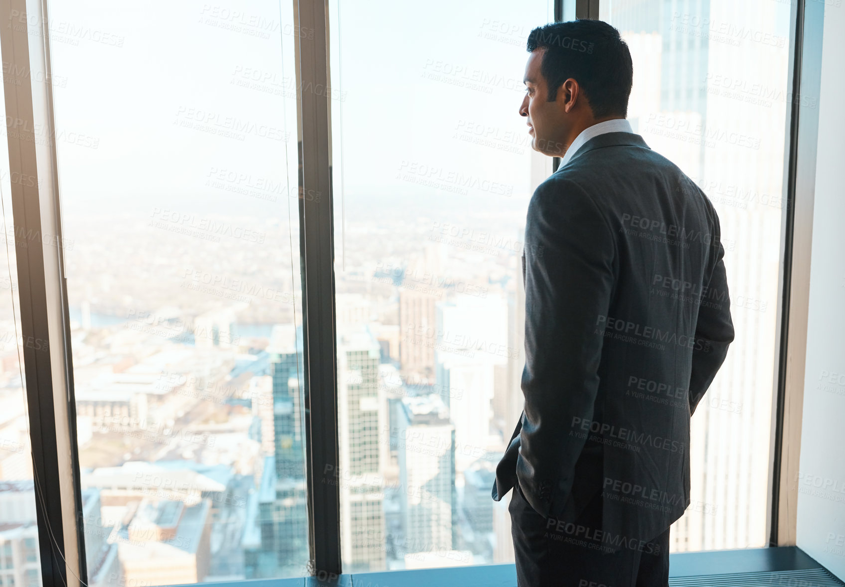 Buy stock photo Shot of a young businessman looking out the window in an office