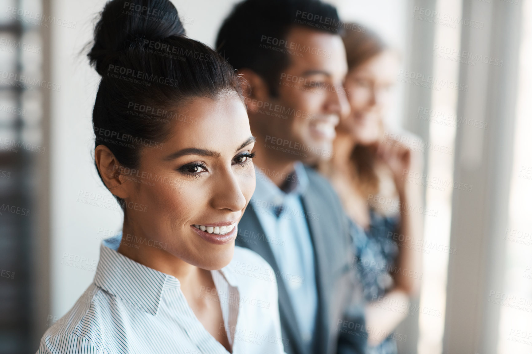 Buy stock photo Shot of a young businesswoman standing in an office with her colleagues in the background