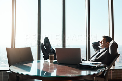 Buy stock photo Shot of a young businessman relaxing with his feet up on a table in an office