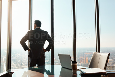 Buy stock photo Rearview shot of a young businessman looking out the window in an office