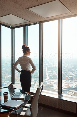 Buy stock photo Rearview shot of an attractive young businesswoman standing with her hands on her hips in the office