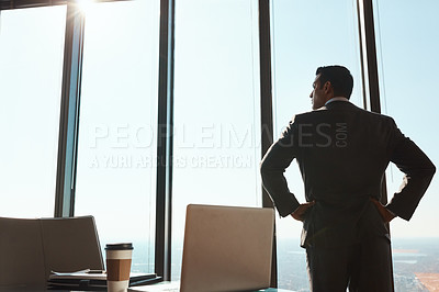 Buy stock photo Rearview shot of a handsome young businessman standing with his hands on his hips in the office