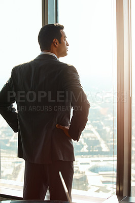 Buy stock photo Rearview shot of a handsome young businessman standing with his hands on his hips in the office