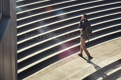 Buy stock photo Shot of a young businessman using a mobile phone while walking through the city