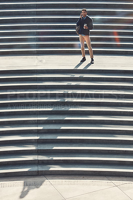 Buy stock photo Shot of a young businessman using a mobile phone while walking through the city