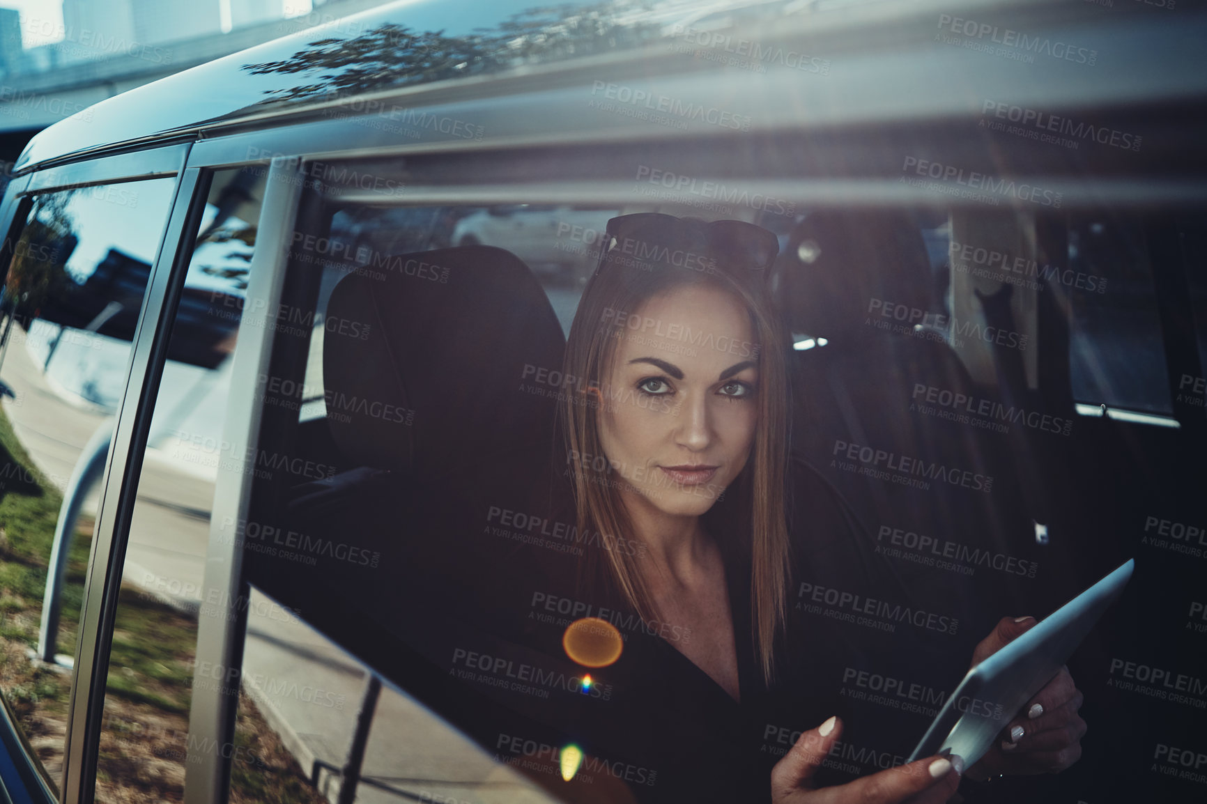 Buy stock photo Shot of a young businesswoman using a digital tablet while traveling in a car